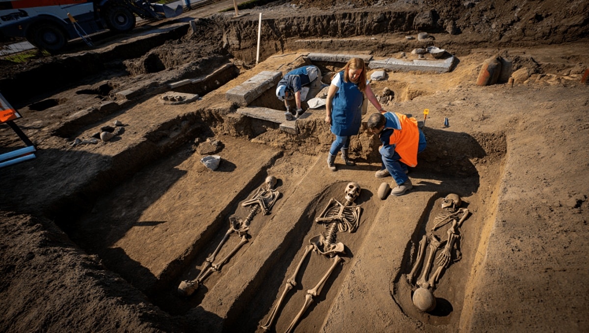 Im Mittelpunkt steht ein großer, halbkugelförmiger Erdblock, der mit Folie und Klebeband gesichert ist. Er befindet sich auf einer weißen Platte auf einem Holztisch. Daneben liegen archäologische Werkzeuge wie Pinsel, Spatel und ein kleiner Mörser. Im Hintergrund sind Labormöbel, Geräte, Schubladen und weitere Arbeitsmaterialien zu sehen. Die Szene spielt in einem modernen Laborraum.